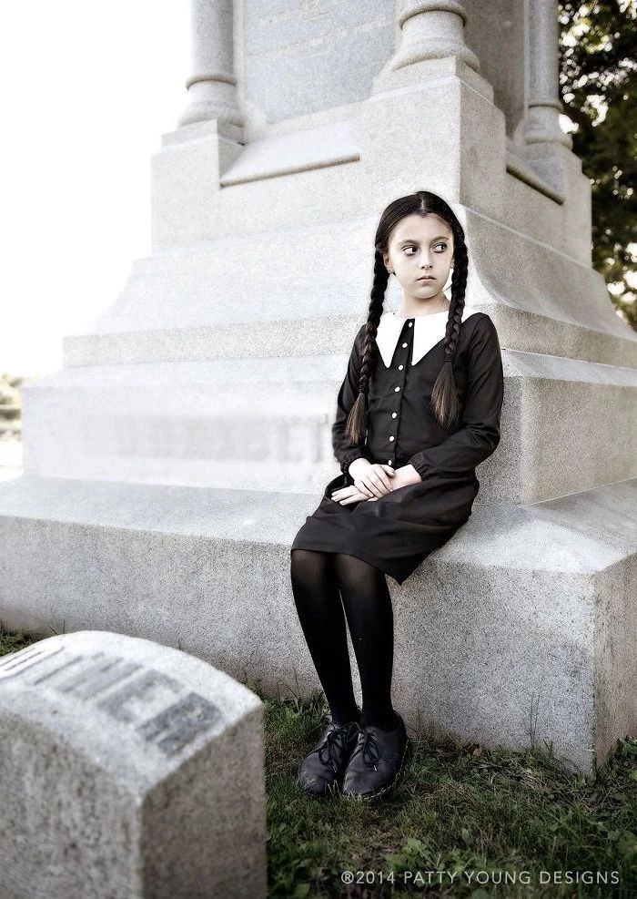 girl sitting on a tombstone, dressed as wednesday addams, halloween costume ideas, addams family inspired costume