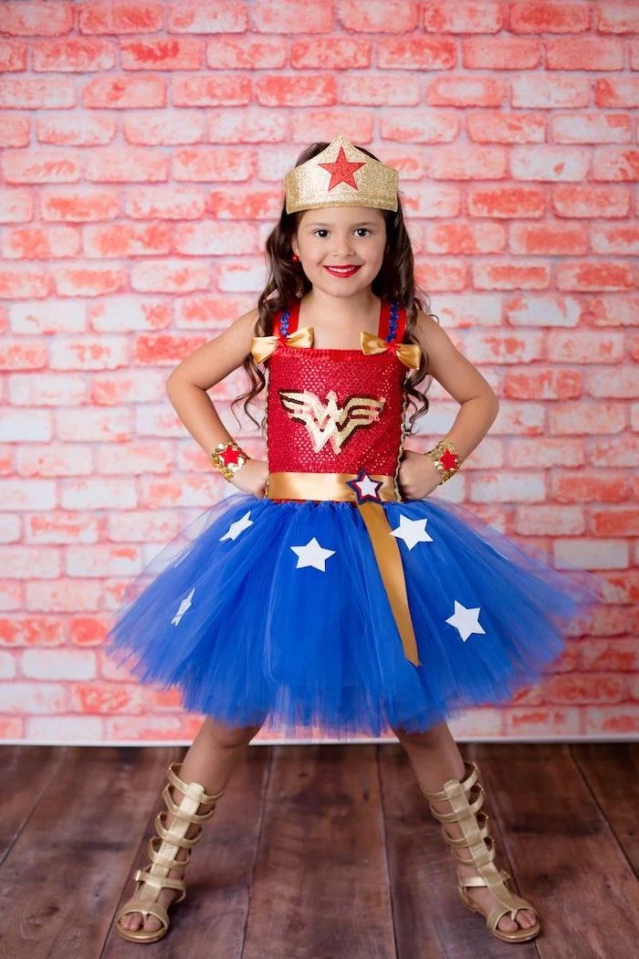 girl dressed as wonder woman, red top, blue tulle skirt, toddler boy halloween costumes, brick wall, gold gladiator sandals