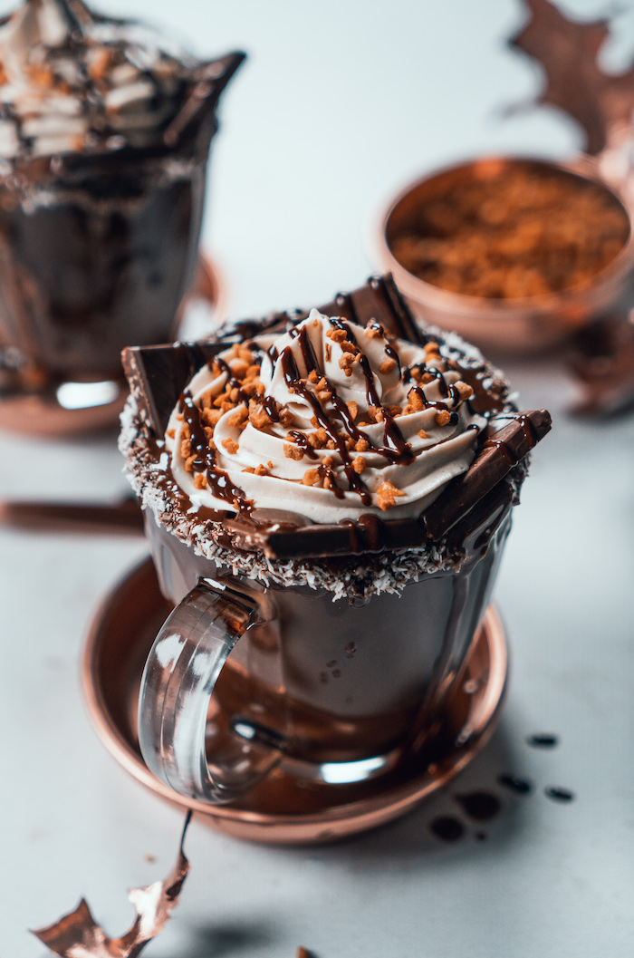 homemade hot chocolate recipe, poured into a glass jar, chocolate bar and cream on top, placed on white surface