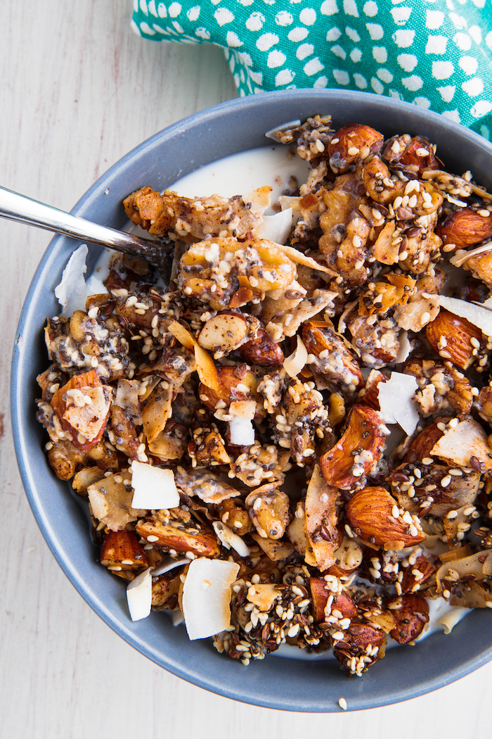 granola with milk, almonds and sesame seeds, coconut flakes, in a grey bowl, quick keto breakfast, wooden table