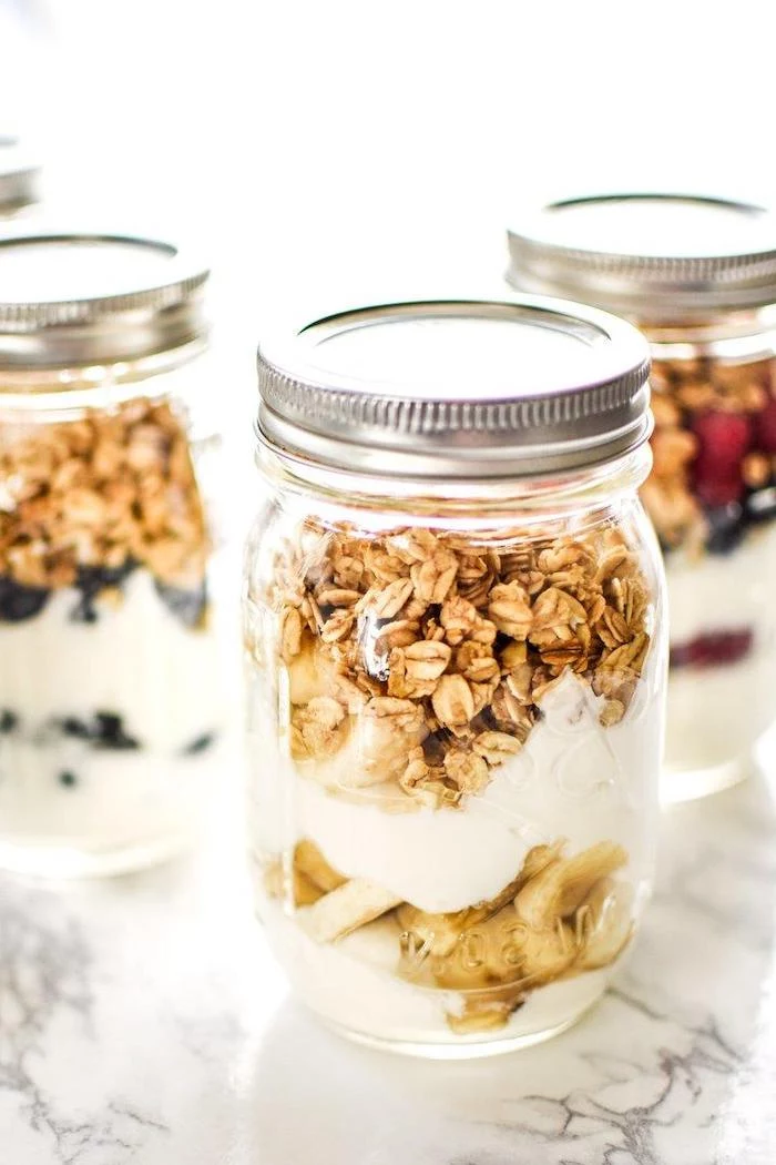 granola and yoghurt, inside mason jars, with different fruits, meal prep, marble countertop