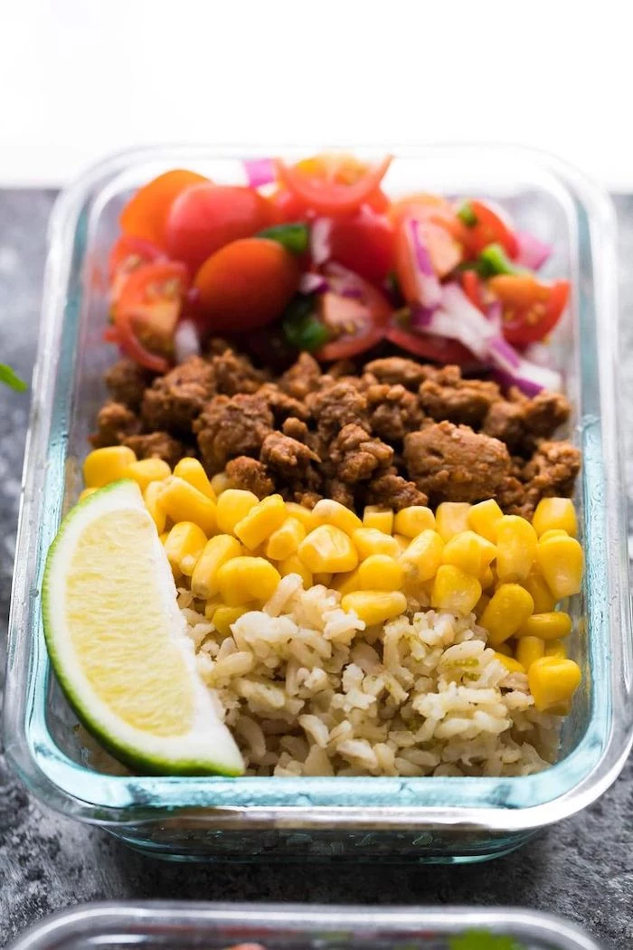 rice and corn, ground turkey, chopped tomatoes and onions, chicken meal prep, lime slice, in a glass container