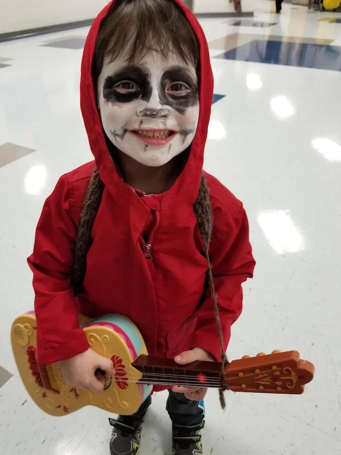 little boy, dressed as miguel rivera, coco movie inspired costume, halloween costumes for girls, holding a guitar, red hoodie