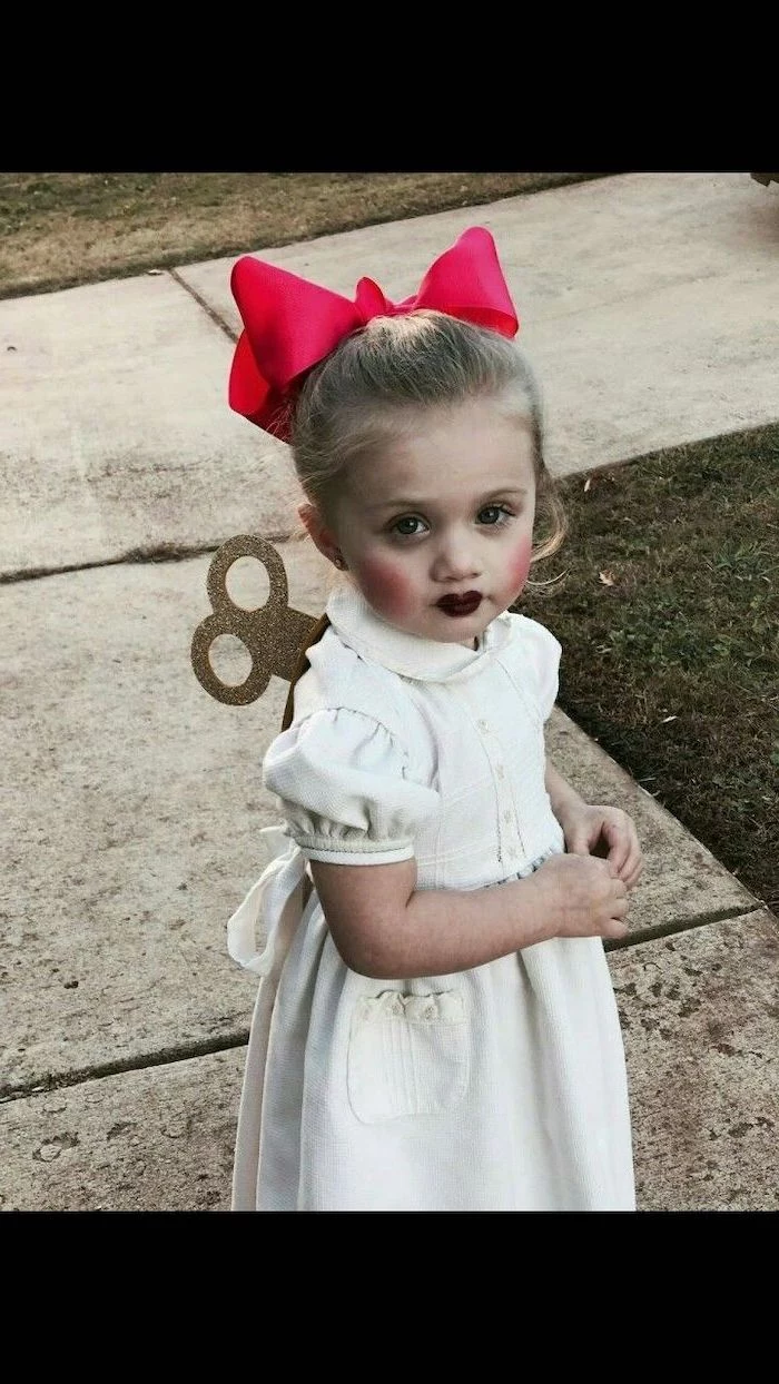 little girl, with blonde hair, dressed as a doll, wearing white dress, red bow, halloween costume ideas for girls