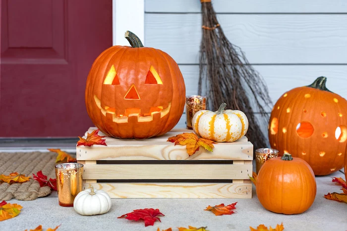 orange pumpkins, with different carvings, pumpkin carving, small pumpkins, arranged around a wooden crate