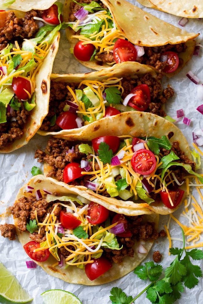 tortilla wraps, filled with beef, cherry tomatoes, ground beef taco recipe, lime slices on the side, cheese on top