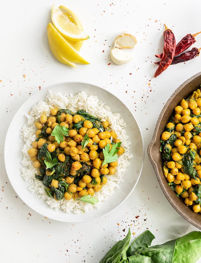 rice with chickpeas and spinach, in a white plate, healthy meal prep, lemon slices, garlic and peppers