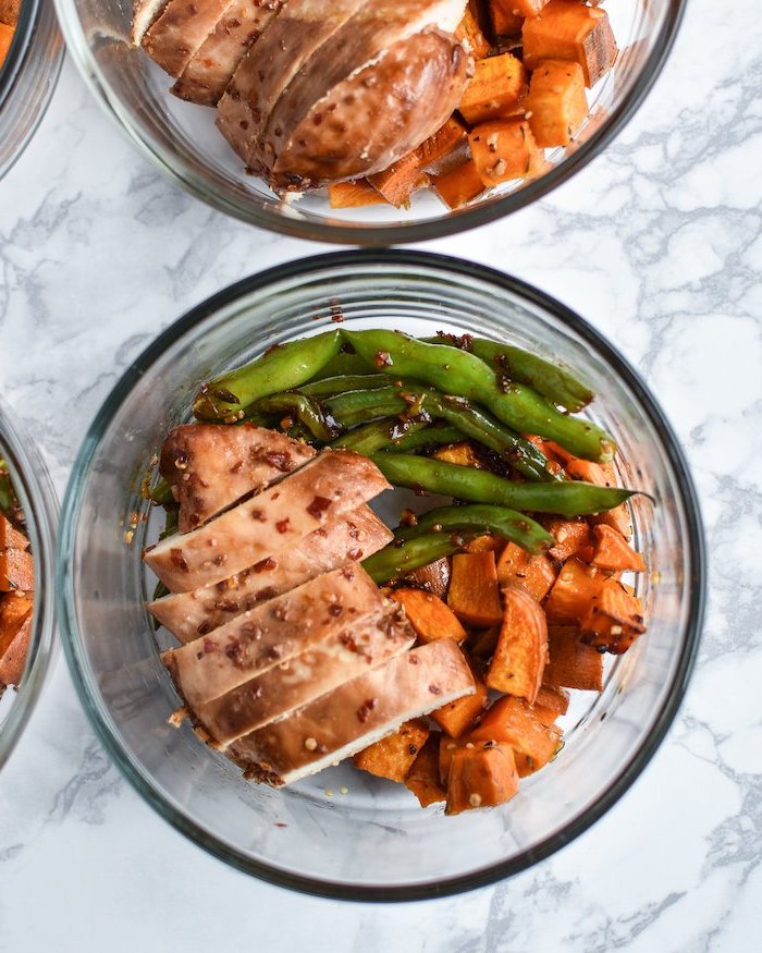 glass bowl, filled with marinated chicken, sesame seeds, beans and sweet potato, meal prep for the week, marble countertop