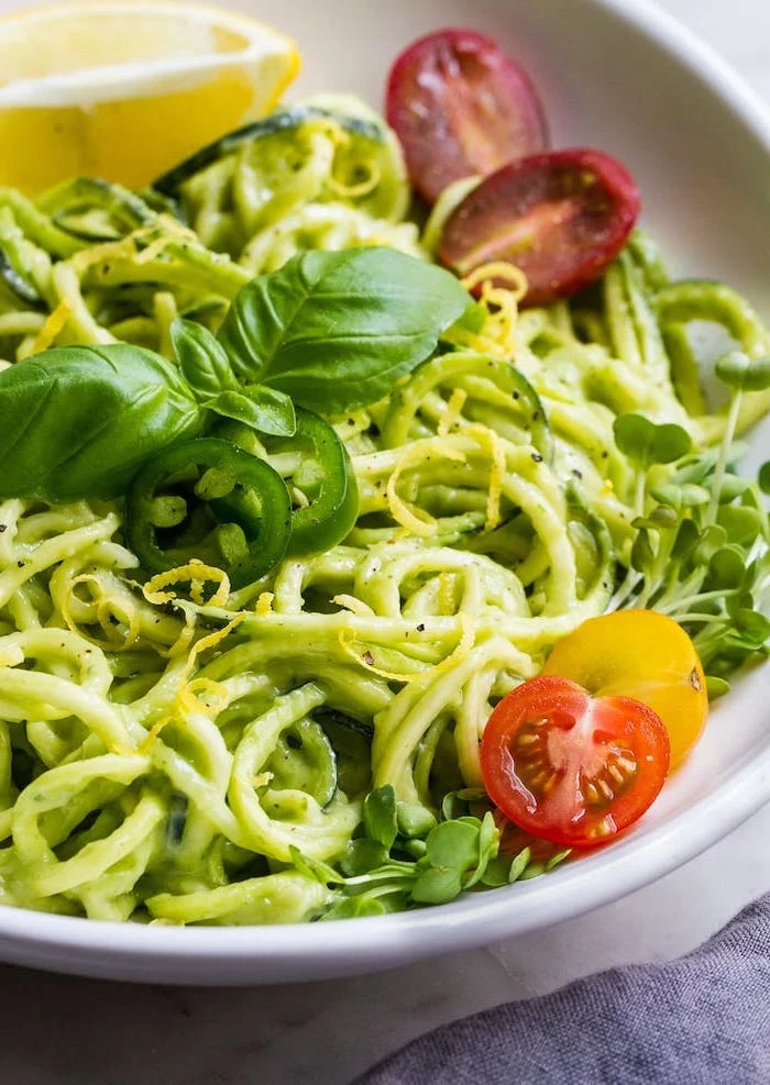 how to spiralize zucchini, cherry tomatoes, chopped peppers, basil on top, zoodles in white plate