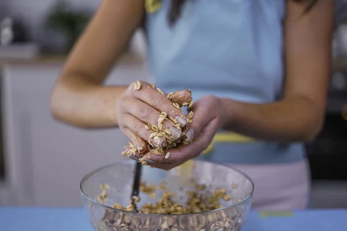 woman shaping cookies, oatmeal cookies, chocolate chip cookies, mix in a glass bowl, wearing a blue apron