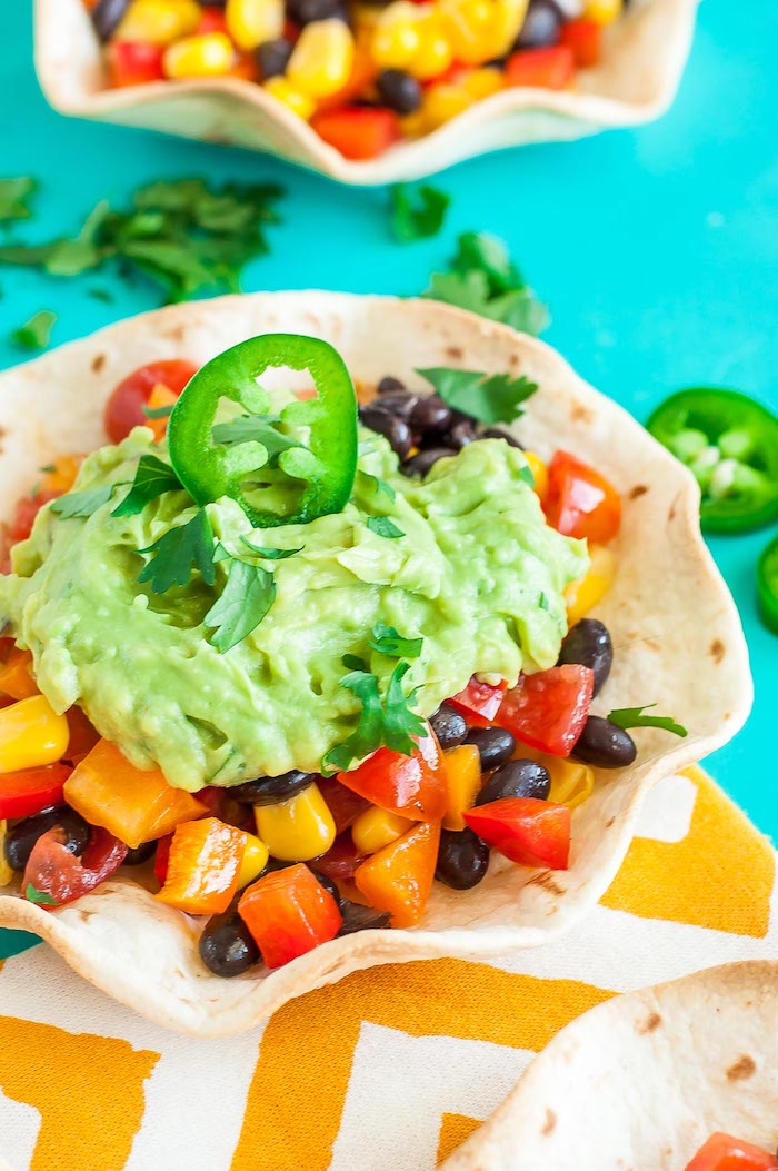 turquoise table, homemade taco sauce, tortilla bowl, filled with corn, chopped vegetables, black beans, guacamole sauce