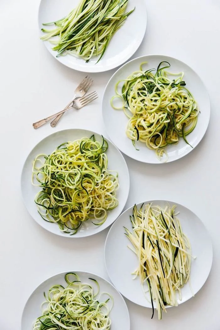 zoodles in five different ways, in white plates, on white table, how to spiralize zucchini, two forks