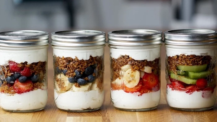 healthy lunch ideas for work, four mason jars, granola and yoghurt, different fruits inside, berries and bananas
