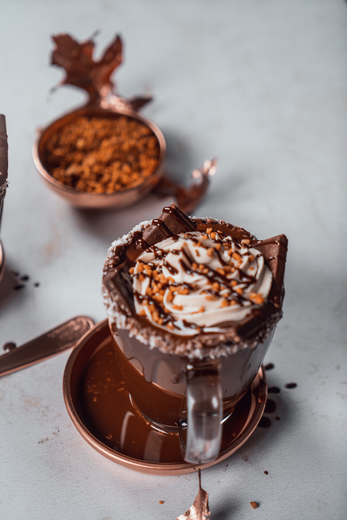 hot chocolate poured into glass mug, coconut shavings and melted chocolate on the rim, cream and chocolate on top