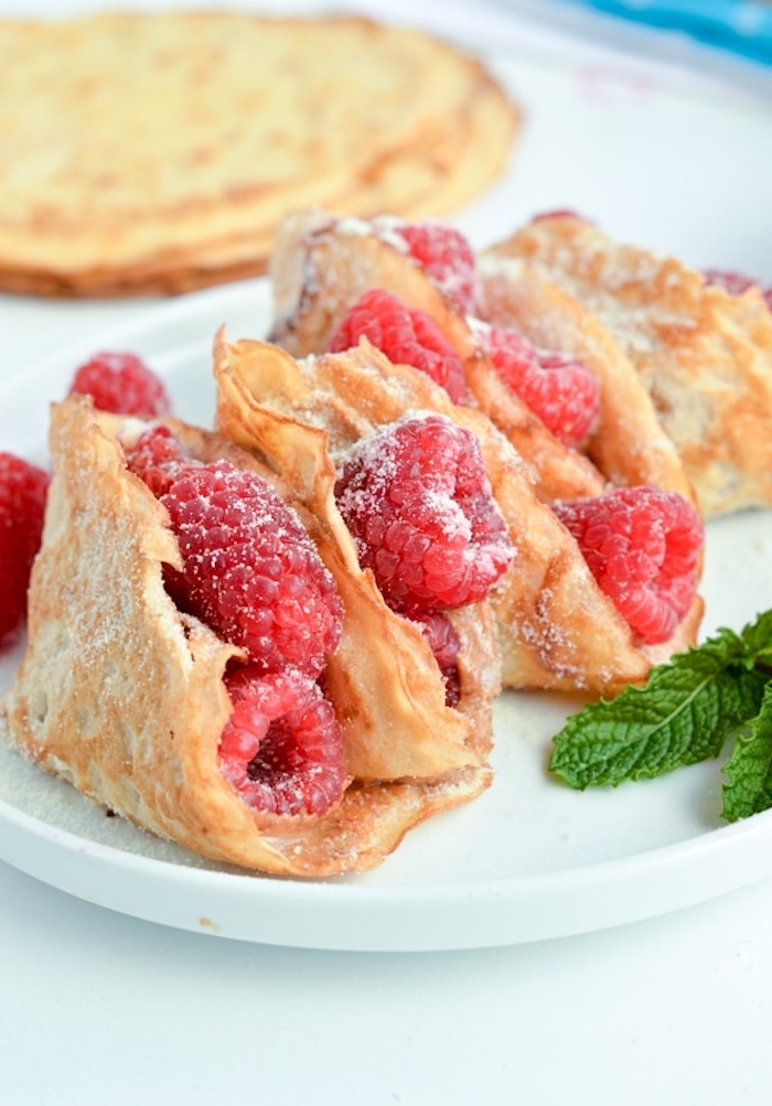 folded crepes, raspberries inside, covered in powdered sugar, coconut flakes, on white plate, keto breakfast