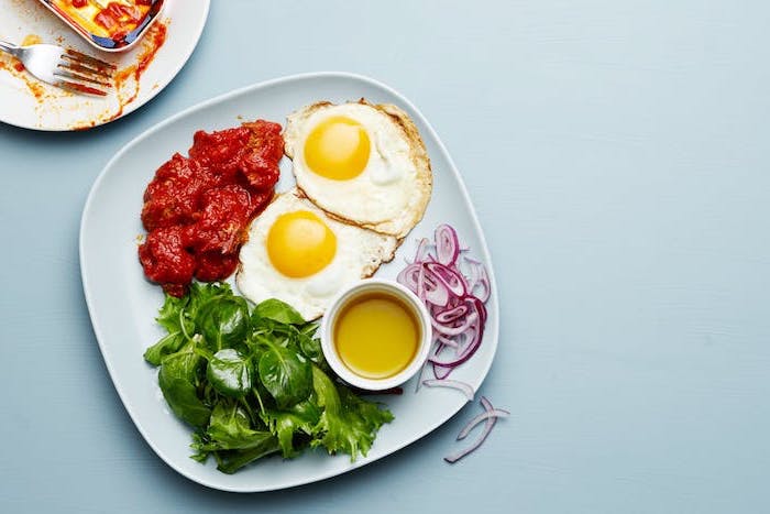 fried eggs, tomato sauce, spinach and onion, on the side, white plate, keto breakfast no eggs, blue table