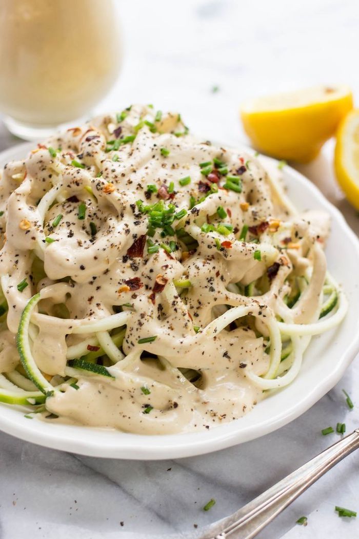 lemon cream sauce, zucchini noodles recipe, chives on top, in a white plate, marble countertop