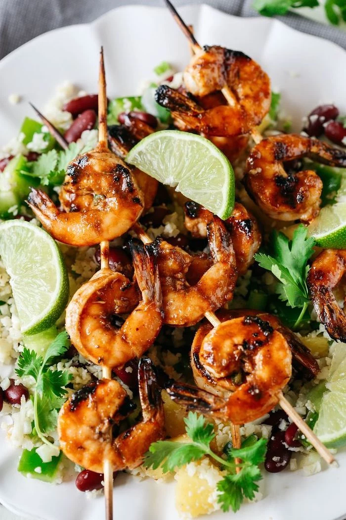 shrimp on wooden skewers, healthy lunch recipes, rise with black beans, lime slices, parsley on the side