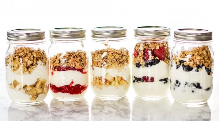 five mason jars, filled with fruits, granola and yoghurt, meal prep, white background, berries and bananas