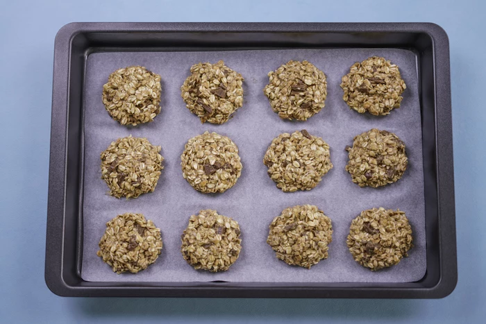 chocolate chip cookie recipe, oatmeal cookies, arranged on a white baking sheet, in a baking tray, blue table