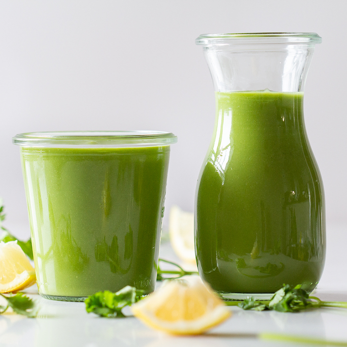 glass and jug, keto breakfast, green smoothie, lemon slices, parsley scattered around, white table