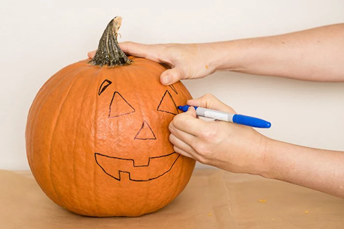 scary pumpkin faces, tracing a face, onto a pumpkin, with a sharpie, white wall
