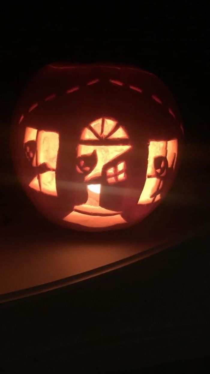 ghosts inside a house, carved into a pumpkin, scary pumpkin carvings, lit by candles, black background