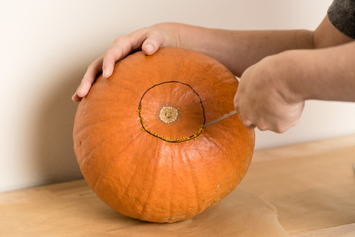 two hands, cutting a hole, into a pumpkin, jack o lantern faces, wooden table, white wall