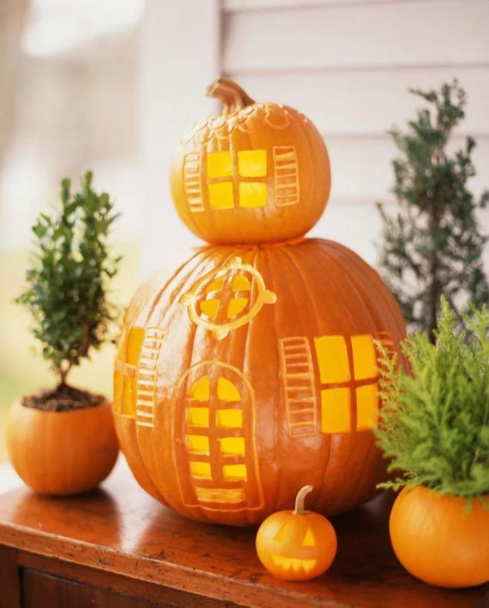 two pumpkins, stacked together, in the shape of a house, scary pumpkin faces, wooden table, potted plants