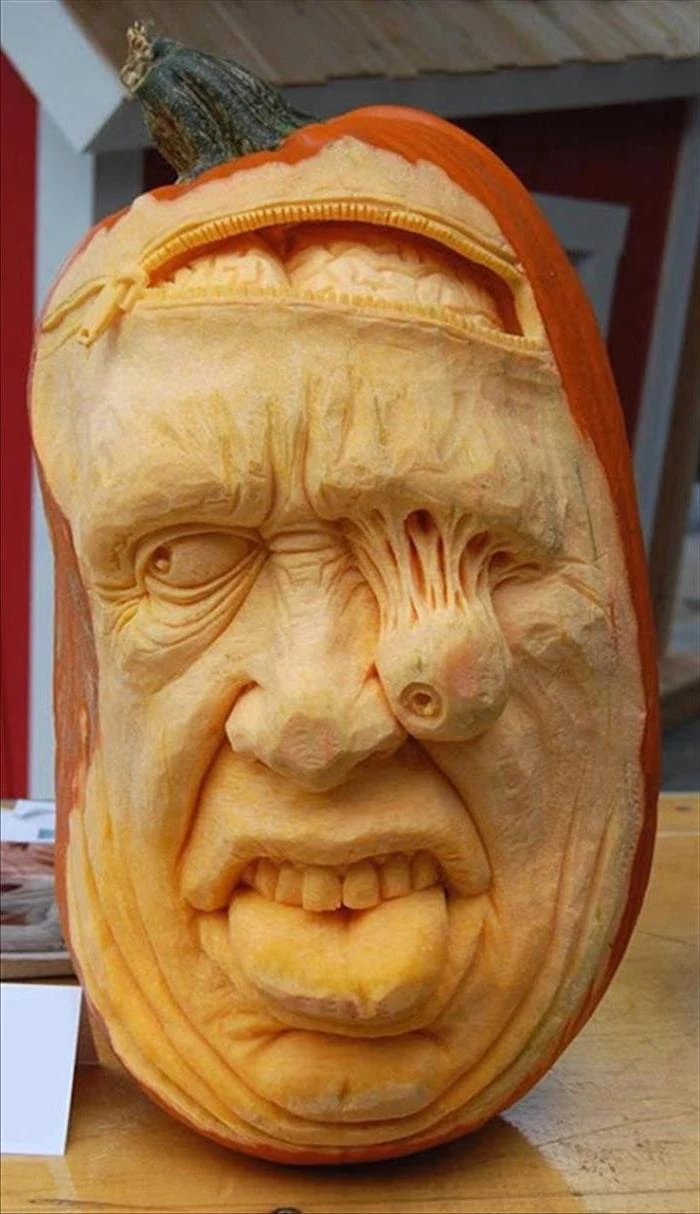 man's face, carved into a pumpkin, falling eye, brains coming out, funny pumpkin carving ideas, wooden table