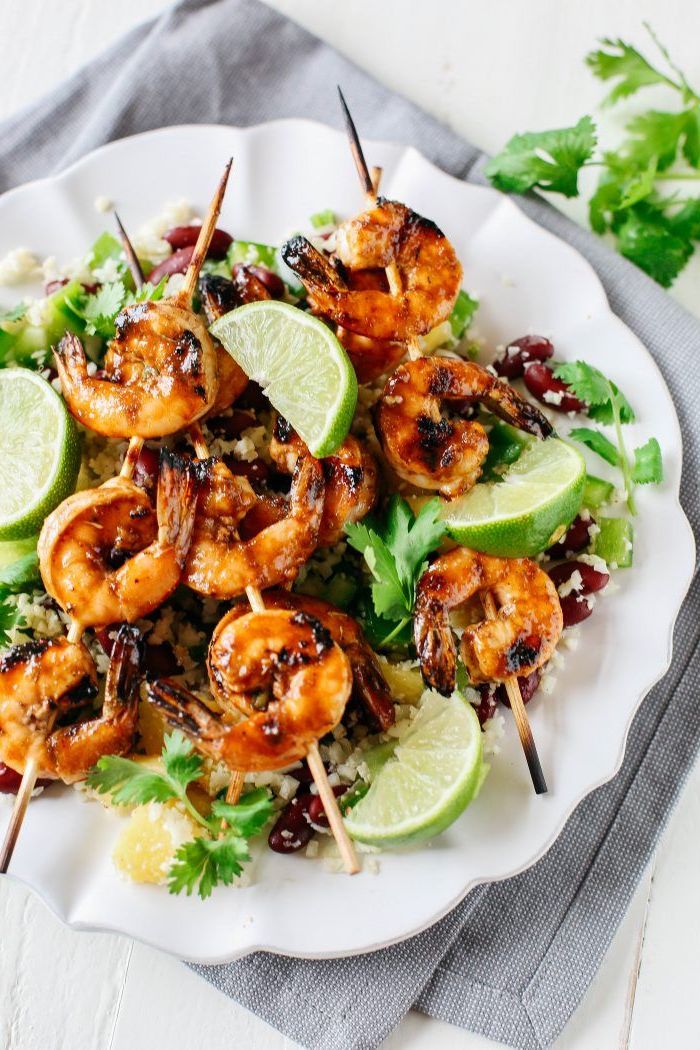 white plate, healthy lunch recipes, shrimp on wooden skewers, rice with black beans, lime slices, parsley on the side