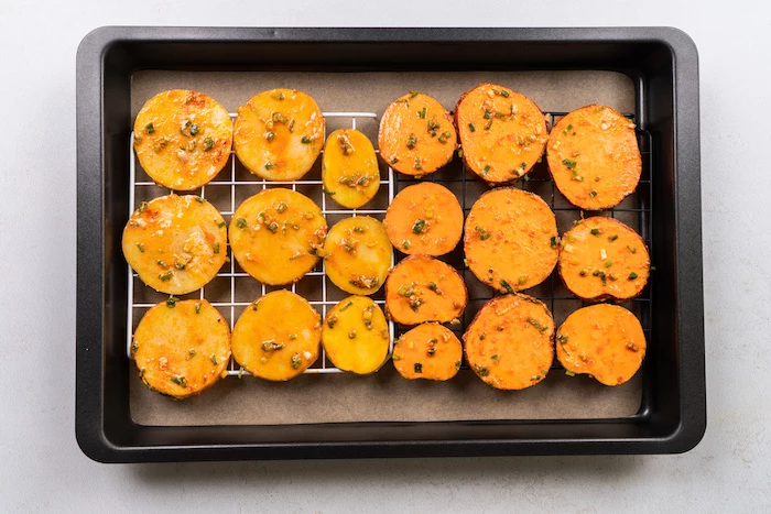 potato and sweet potato slices, arranged on metal rail, homemade potato chips recipe, in paper lined baking sheet