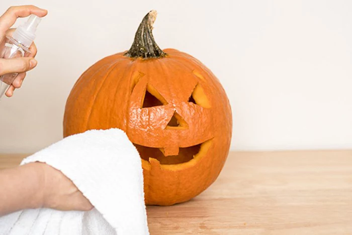 spraying the pumpkin, scary pumpkin faces, white towel, wooden table, white wall