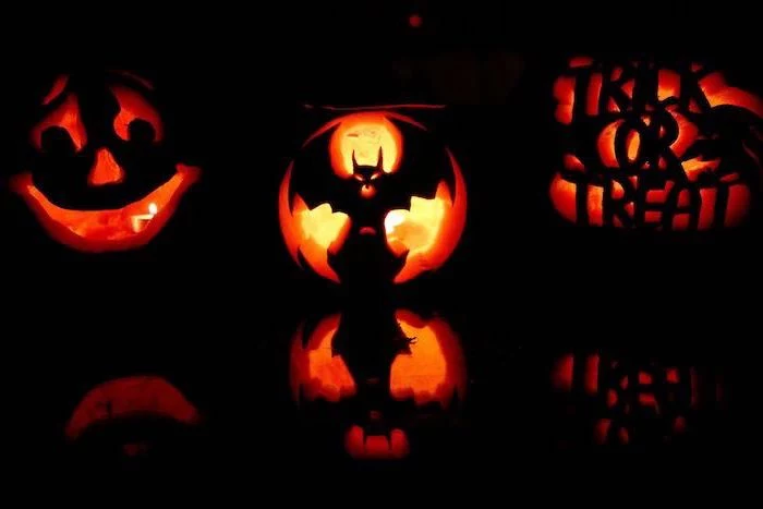 three pumpkins, with different carvings, lit by candles, pumpkin carving designs, black background, pumpkin inside pumpkin carving patterns
