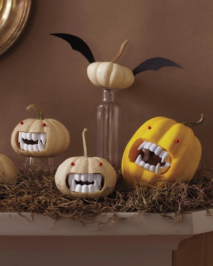 four pumpkins, arranged on a mantle, pumpkin carving designs, plastic vampire teeth, red eyes, glued to them