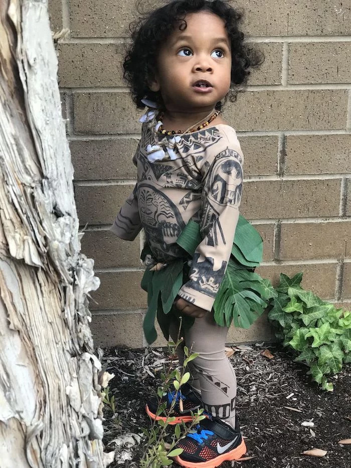 toddler girl halloween costume, dressed as maui, moana movie inspired, black curly hair, brick wall