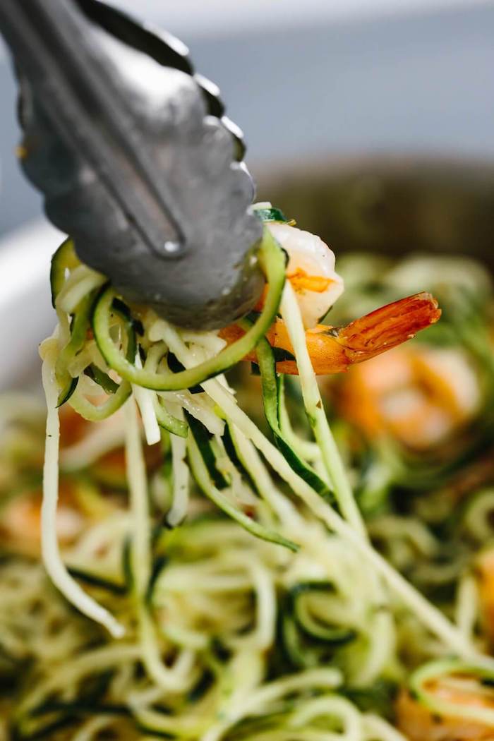 silver tongs, holding zoodles with shrimp, zucchini noodles spaghetti, blurred background
