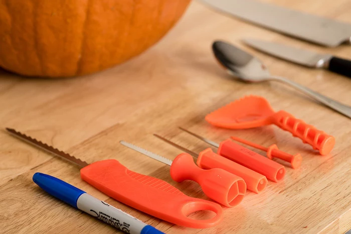 different tools, for pumpkin carving, arranged on a wooden table, jack o lantern faces, orange pumpkin