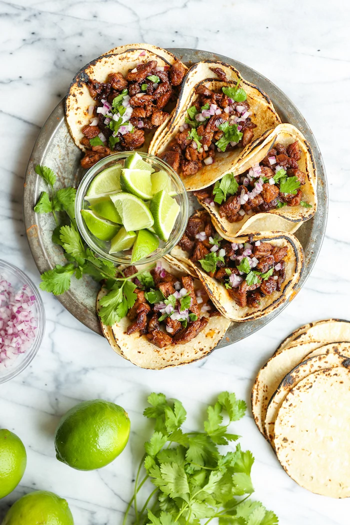 five tacos, tortilla wraps, filled with beef, how to make taco meat, arranged on a silver plate, lime slices, in a glass bowl