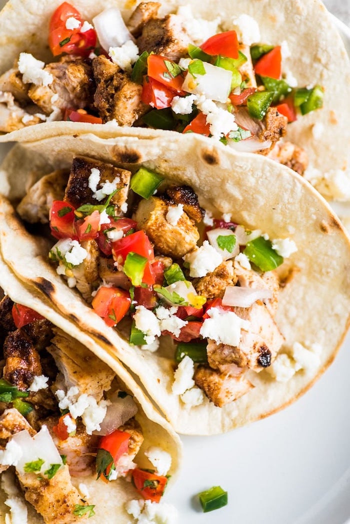 tortilla wraps, filled with chicken fillet, chopped tomatoes, hard shell taco, white plate