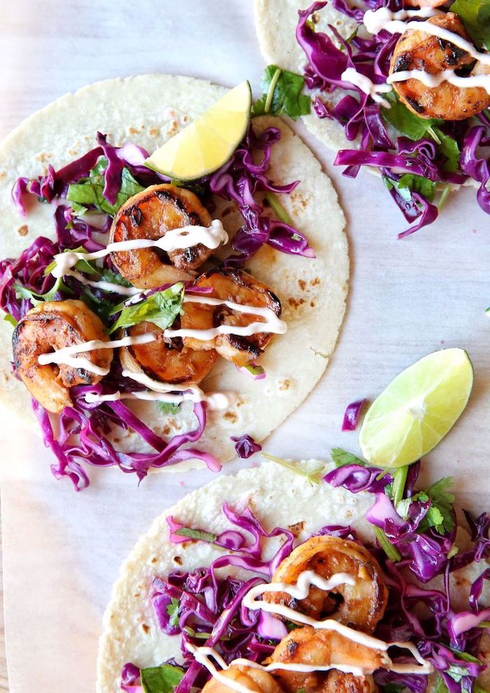 taco ingredients, tortilla wraps, filled with cabbage, fried shrimp, lime slices on the side