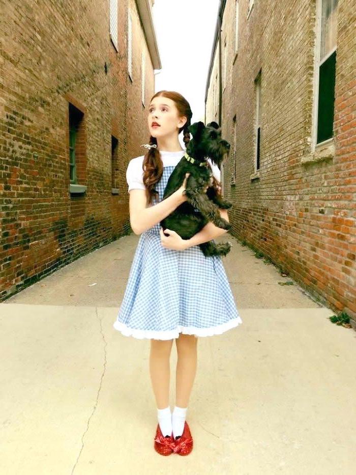 girl dressed as dorothy, wizard of oz inspired, braided hair, red shoes, funny halloween costumes for kids, holding a dog