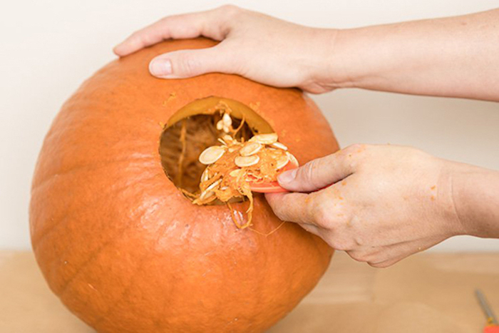 two hands, taking out the insides of a pumpkin, jack o lantern faces, orange pumpkin, white wall