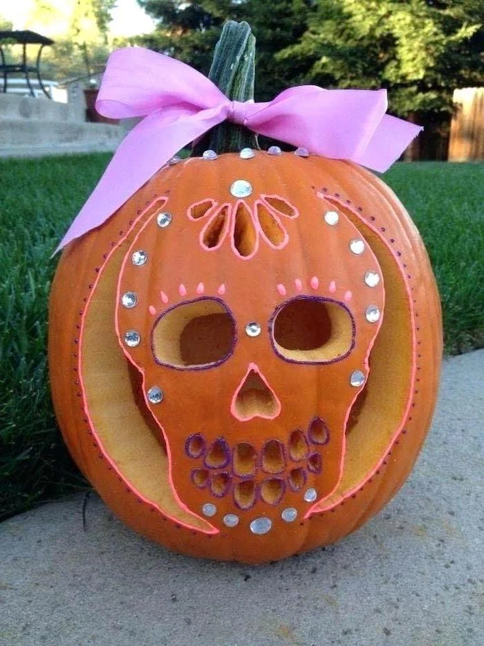 carved pumpkin, with a pink bow, rhinestones glued to it, halloween pumpkin carvings, skull shape