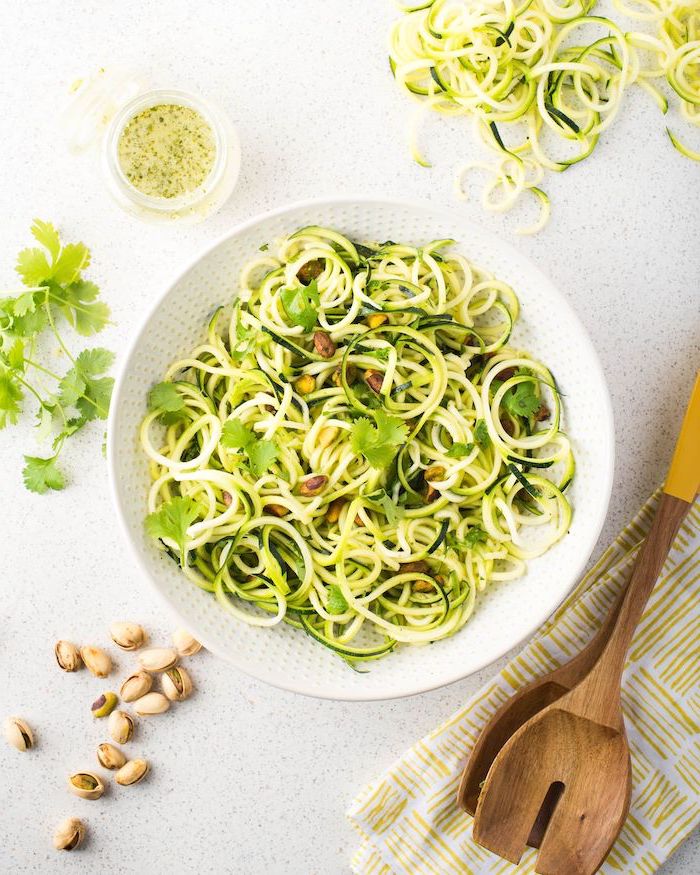 what are zoodles, white bowl, zucchini noodles, parsley on top, wooden spatulas, white table