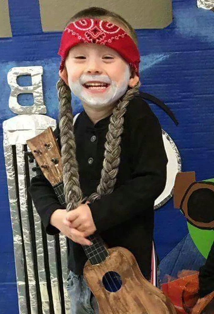 little boy, dressed as willie nelson, holding a guitar, funny halloween costumes for kids, two braids, red bandana