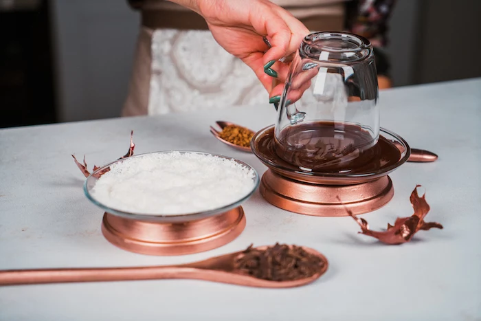 glass jar dipped into melted chocolate, coconut shavings in another bowl, homemade hot chocolate recipe, placed on white surface