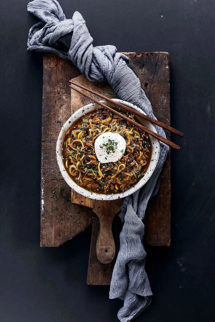grey cloth, wooden cutting board, zucchini noodles, asian recipe, wooden chopsticks, white bowl