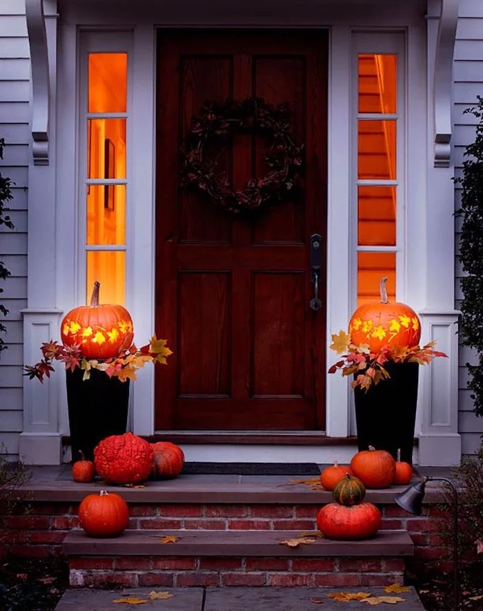 two pumpkins, lit by candles, smaller pumpkins, arranged on stairs, in front of a door, halloween pumpkin carvings