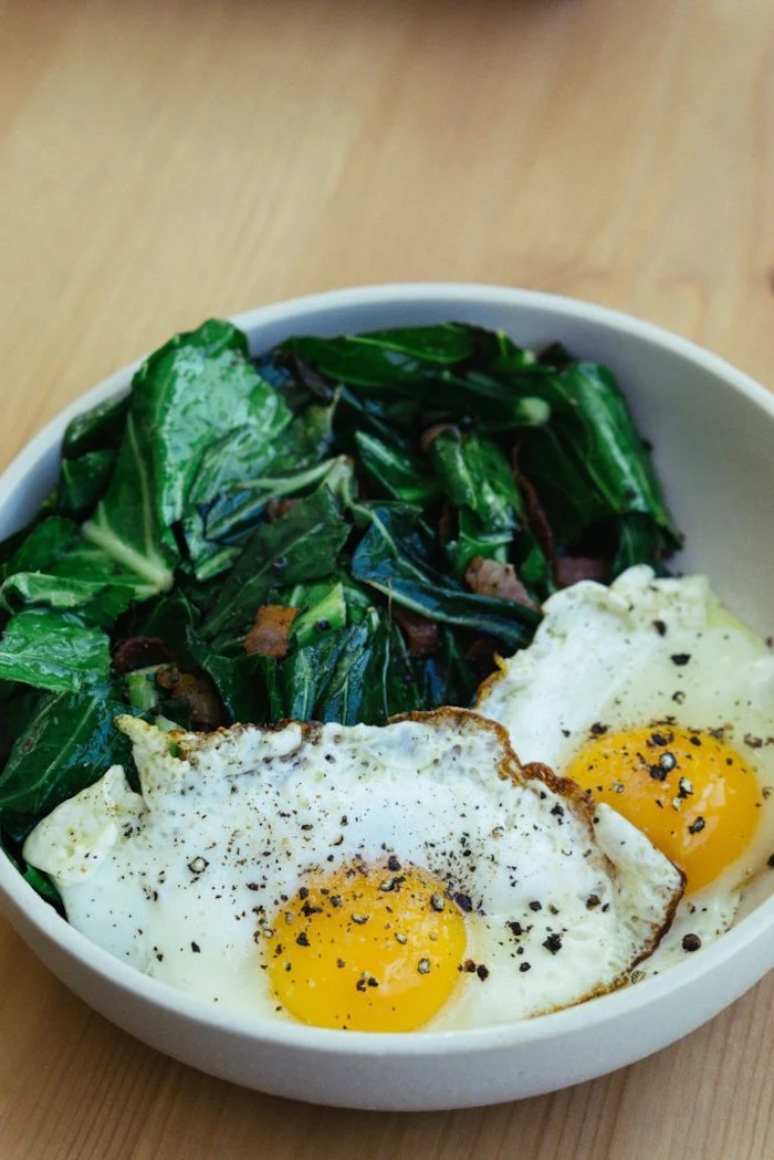 spinach and bacon, on the side, fried eggs, in a white bowl, easy keto meals, wooden table